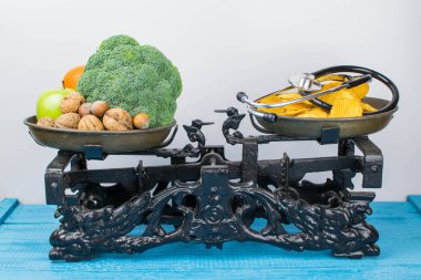 Sağlıklı meyve ve sebze, patates cipsi ve bir steteskop ölçeklerde karşı. Doğru beslenme ve kilo kaybı