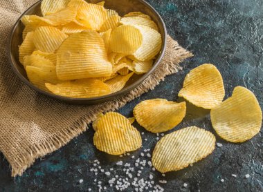 Eski mutfak masasında bir hasır kase gevrek patates cipsi