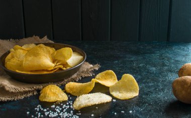 Eski mutfak masasında bir hasır kase gevrek patates cipsi