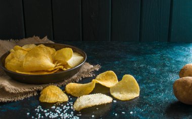 Eski mutfak masasında bir hasır kase gevrek patates cipsi