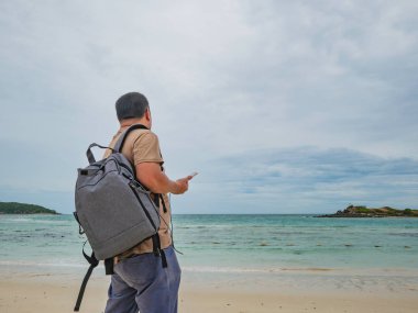 Asyalı şişman backpacker tatil zamanı tribünde kullanım cep telefonu güzel gökyüzü ile pastoral plaj üzerinde iken. Samae San Adası Tayland. Yaz konsepti.