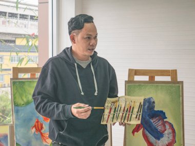 Sınıf, Balık kavramı boya fırçası kullanmayı öğretme yakışıklı genç Asyalı adam veya su renk sanatçı