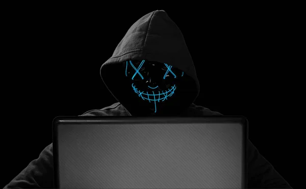 hacker with glowing mask behind notebook laptop in front of isol