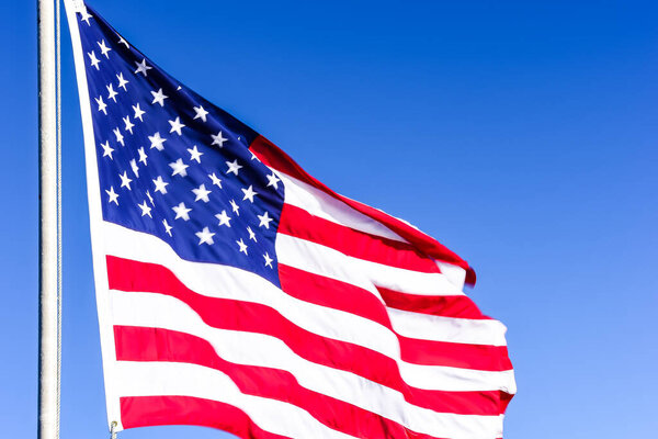 American flag is flowing in the wind on blue sky background.