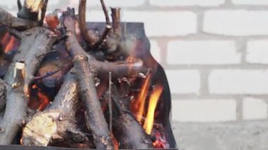 Ateş yakar. Farklı boyutta yakacak odun. Yangın sinirlendiren. Yoğun bir gri duman var. Yakacak odun kapatın. Tuğla duvarın arkasında.