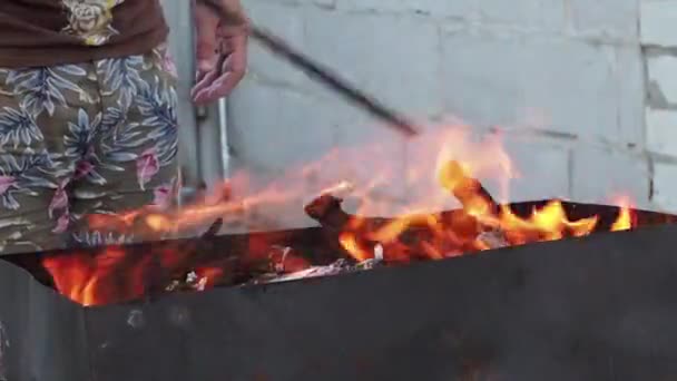 男は燃える薪を移動します 男は火鉢で柴に金属棒をミックスします 火の凝り固まった — ストック動画