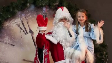 Güzel kız Snegurochka ve babası Don Noel Baba bir el salla. Bir çocuk Noel arifesinde tatil. Yılbaşı karakterleri büyük saat arka planı.