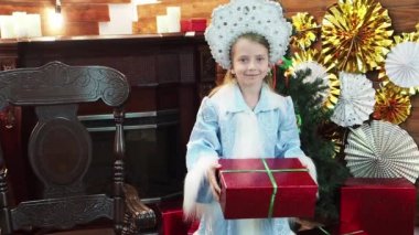 Küçük kız bir şömine yakın ahşap bir sandalyede oturuyor. Güzel güzel kız peri masalı yeni yıl'ın Noel karakter bize bir hediye kapalı şık kutusunda uzanır. Küçük kar kraliçesi.