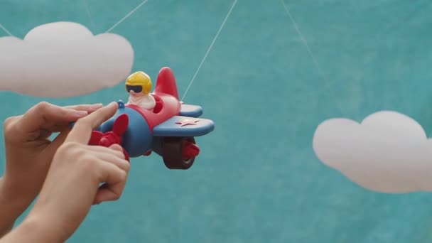 女性の手はおもちゃの飛行機パイロットとネジを回転させます 白い雲と青い背景 番目のおもちゃの飛行機が経ちます 女性が手でおもちゃを保持します — ストック動画