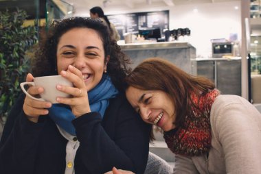 İki kadın arkadaş (anne ve kızı) bir şaka ve bir sohbet ve bir fincan kahve ya da çay keyfi, gülen ve bir kafede gülümseyen