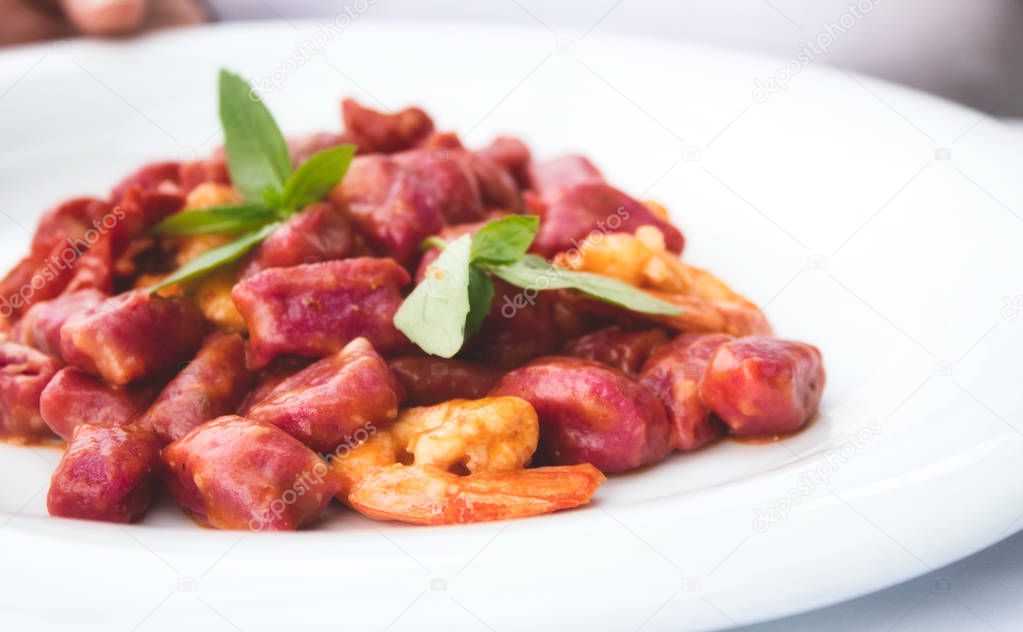 Beetroot gnocchi and prawns garnished with mint on a white plate