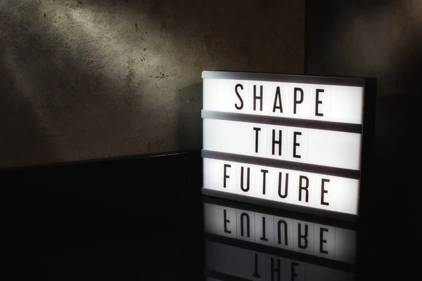 Shape the future motivational message of progress on a light box in a cinematic moody background