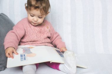 Küçük kız bebek beyaz bir kanepe üzerinde bir resimkitap okuma