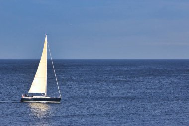 Yelkenli açık mavi gökyüzü ve arka planda ufuk ile denizde yüzüyor.