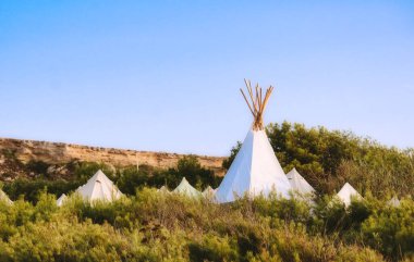 Açık mavi bir gökyüzünün altında beyaz çadır çadırları (veya wigwams) kamp kurdu.