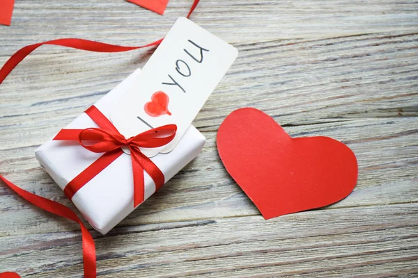 white gift box with red bow and hearts on white wooden background with gold bokeh, Valentines day gift, tag I love you