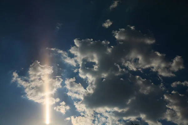 Yellow rays of the sun easily cut through a white cloud on a blue sky