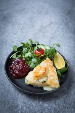 Camembert en croute peynirli puf böreği içinde kırmızı reçel, salata, sebze ve limon dilimi gri grunge arka plan üzerinde siyah bir tabakta servis.