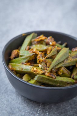 Hintli bir garnitür siyah kase ve gri arka plan, yakın çekim. Vejetaryen bamya, siyah bir kabın içinde kızarmış bhindi kızarmış. Kızarmış bhindi Hint baharat ile.