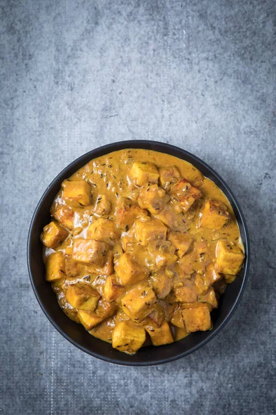 Malai paneer Indian cheese curry in a large black bowl with a top view and with a grey background. Thick creamy paneer curry in the center. Vegetarian Indian curry.