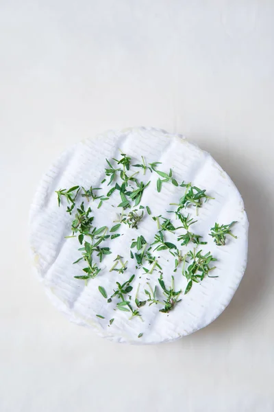 Whole camembert with fresh herbs and fresh thyme on top. Round French cheese at the center with a white background. Wheel of camembert. Wheel of brie.