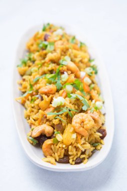 Baharatlı deniz ürünleri uzun görünümünü pirinç yemek sebze, fındık ve ananas ile kızarmış. Turuncu deniz ürünleri paella beyaz bir plaka üzerinde beyaz bir arka plan ile.