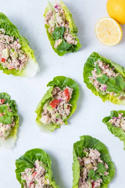 Lettuce tuna wraps. Lettuce leaves filled with healthy tuna salad with lemon in background on a white surface. Green tuna salad recipe.