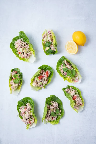 Tuna lettuce wraps on top of a white surface with lemon on a light background.  Top view with many tuna salad lettuce wraps.