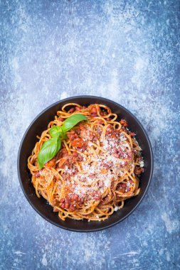 Üstten Görünüm vegan spagetti bolognaise veya bolognese bir koyu siyah kase ve bir aydınlık gri arka plan. Taze fesleğen ile tepesinde.