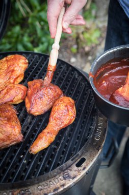 Tavuk parçaları bir ızgara bir Barbekü fırçayla üstüne kötek. Kişi puttinf Barbekü sos ızgara tavuk üzerinde fırça ile. Açık arka plan.