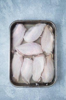 Bir brininig çözüm ve metalik bir tepsi üzerinde gri bir arka plan brined tavuk burnu. Tavuk parçalarını brining.