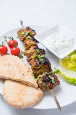 Beyaz bir tabak ta taze pide, marul, domates ve yoğurt ile metalik barbekü şişler kuzu kebaplar. Açık arka plan.