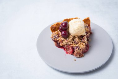 Vanilyalı dondurma ve gri bir tabak üzerinde taze kiraz bir kepçe ile pişmiş kiraz pasta dilim ön görünümü. Açık arka plan.