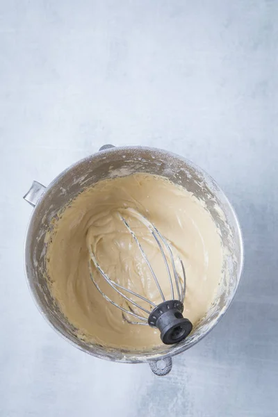 Cake batter inside a deep bowl with a whisk. Light grey background.