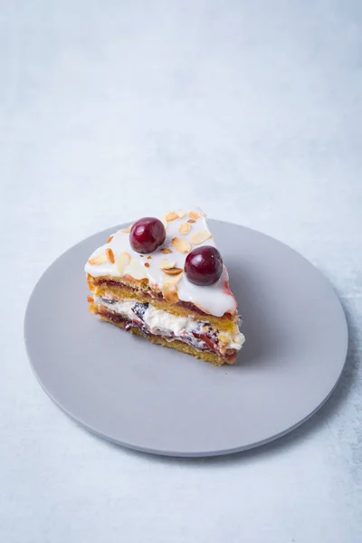 Side view of cake slice of cherry cake on a grey plate and a light background.