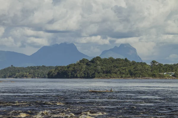\'Rio Negro\' river. Small canoe passing. In the background the Amazon forest and a mountain called \'Sleeping beauty\'. Sky with sun and clouds. So Gabriel da Cachoeira, Amazon / Brazil