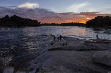 Renkli turuncu ve kırmızı günbatımı 'Rio Negro' River. İnsanlar kayalarda silüeti. Amazon yağmur ormanları. Yani Gabriel da Cachoeira, Amazonas / Brezilya