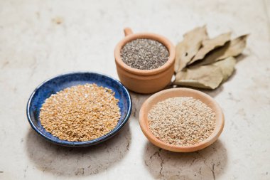 Çanak çömlek ile kompozisyon içeren chia tohum, linum tohum ve susam kase. Laurel Nobilis yapraklar. Mermer yüzey.