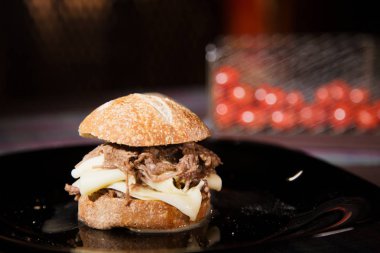 Etli sandviç ve domates arka planda siyah bir tabak içinde bir ekmek.