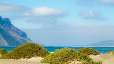 Plaj ve Dağlar - Caleta de Famara 'nın güzel kıyıları, Lanzarote Kanarya Adaları. Caleta de Famara 'daki plaj sörfçüler arasında çok popüler..