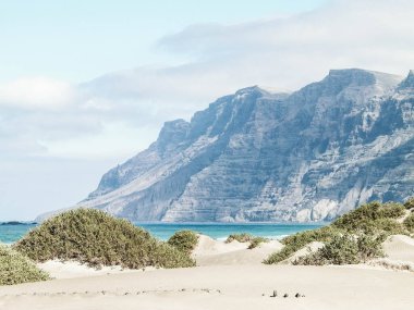 Plaj ve Dağlar - Caleta de Famara 'nın güzel kıyıları, Lanzarote Kanarya Adaları. Caleta de Famara 'daki plaj sörfçüler arasında çok popüler..