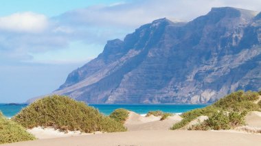 Plaj ve Dağlar - Caleta de Famara 'nın güzel kıyıları, Lanzarote Kanarya Adaları. Caleta de Famara 'daki plaj sörfçüler arasında çok popüler..