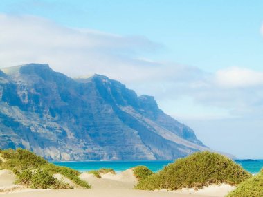 Plaj ve Dağlar - Caleta de Famara 'nın güzel kıyıları, Lanzarote Kanarya Adaları. Caleta de Famara 'daki plaj sörfçüler arasında çok popüler..