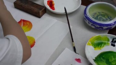 Bir ressam Çin tabloları yapıyor ve onları palete boyuyor.