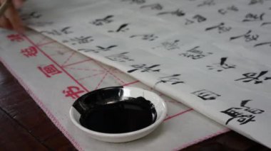 Bir kaligraf yazı hazırlıyor, bir fırçayı mürekkebe batırıyor.