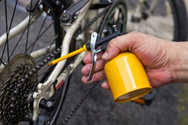 Bisikletin dişlilerini yağ tenekesiyle yağlayan bir insan.