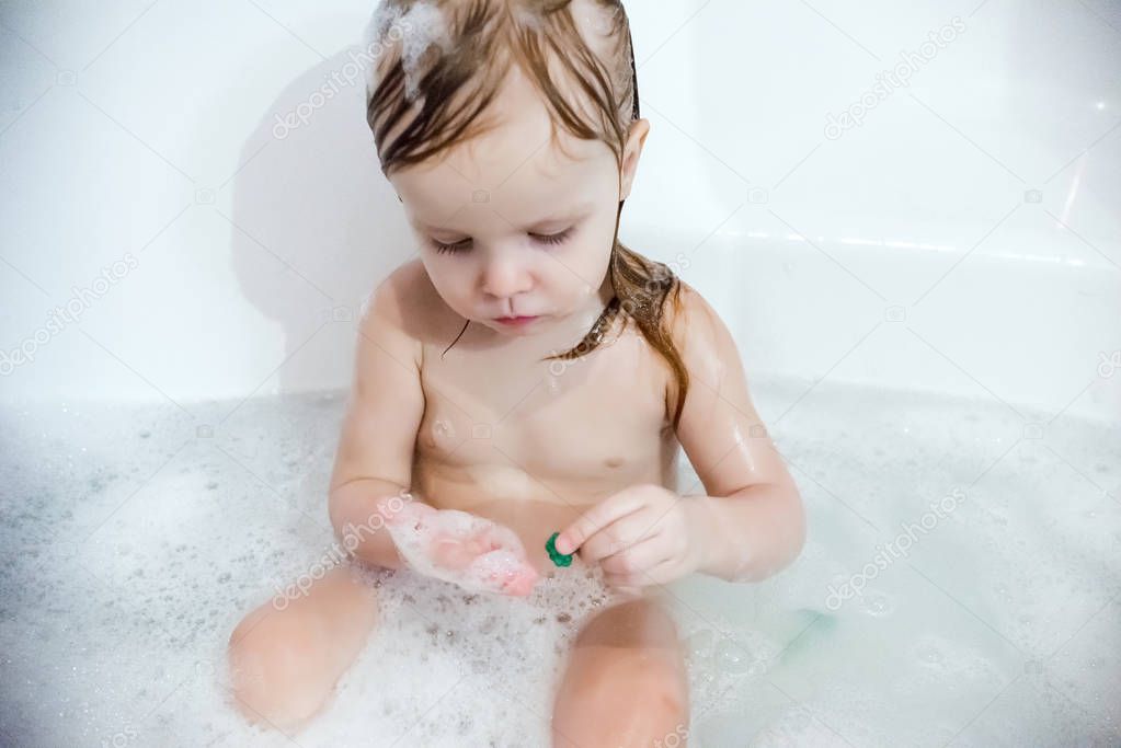 Blonde girl taking bubble bath in white bathroom