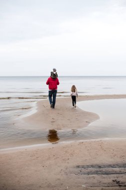 sıcak giysiler giyen ve kumlu sahilüzerinde yürüyen küçük kızları ile baba 
