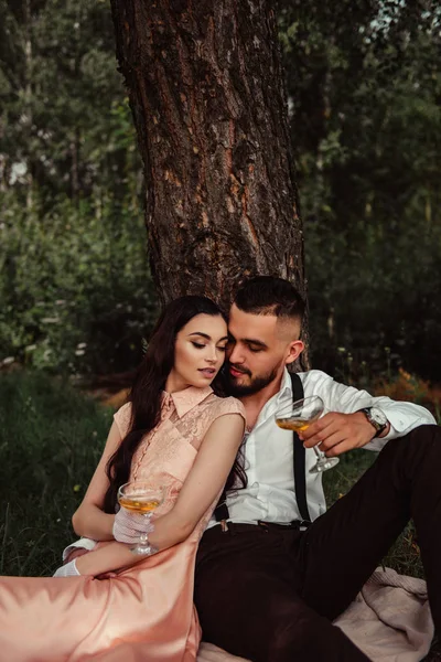 浪漫夫妇喝白葡萄酒从酒杯 而坐在野餐在夏天的森林 — 图库照片