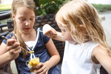 güneşli bir günde kafede birlikte otururken dondurma yiyen sevimli küçük kız kardeşler 
